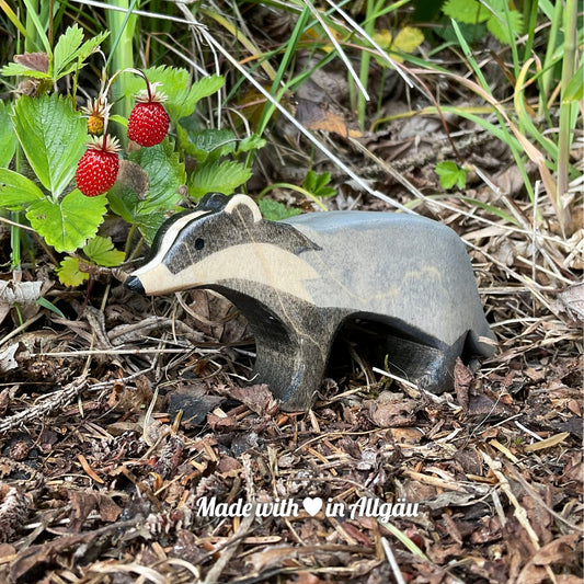 Handgefertigte Dachs-Fähe von Allgäuer Holztiere, grau und schwarz bemalt mit pflanzlichen Farben, stehend auf Waldboden, aus bayerischem Ahornholz gefertigt, nachhaltig produziert im Allgäu und für Kinder ab 3 Jahren geeignet.