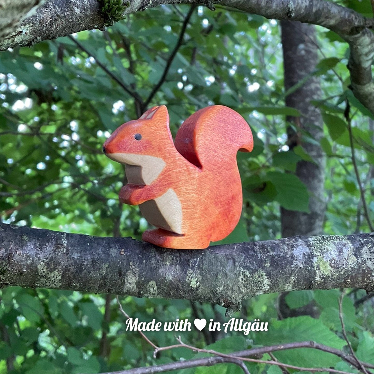Handgefertigtes Holzspielzeug Eichhörnchen weiblich von Allgäuer Holztiere, braun bemalt mit pflanzlichen Farben, sitzend auf einem Ast in natürlicher Umgebung, aus bayerischem Ahornholz gefertigt, nachhaltig produziert im Allgäu und für Kinder ab 3 Jahren geeignet.