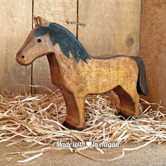 Handgefertigtes Holzspielzeug Pferd Haflinger Stute von Allgäuer Holztiere, stehend auf Holzspänen im Hintergrund raues Holz, aus bayerischem Ahornholz gefertigt, mit pflanzlichen Farben braun und schwarz bemalt, nachhaltig im Allgäu produziert und für Kinder ab 3 Jahren geeignet.