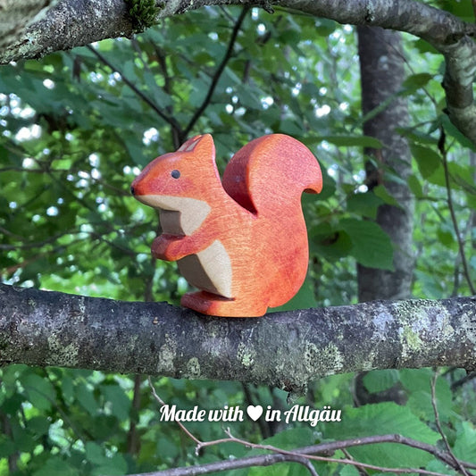 Handgefertigtes Holzspielzeug Eichhörnchen weiblich von Allgäuer Holztiere, braun bemalt mit pflanzlichen Farben, sitzend auf einem Ast in natürlicher Umgebung, aus bayerischem Ahornholz gefertigt, nachhaltig produziert im Allgäu und für Kinder ab 3 Jahren geeignet.