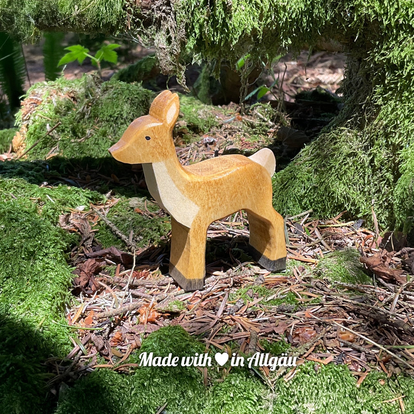 Handgefertigtes Holzspielzeug Reh Ricke von Allgäuer Holztiere, braun und schwarz bemalt mit pflanzlichen Farben, stehend auf Waldboden und Moos in natürlicher Umgebung, aus bayerischem Ahornholz gefertigt, nachhaltig produziert im Allgäu und für Kinder ab 3 Jahren geeignet.