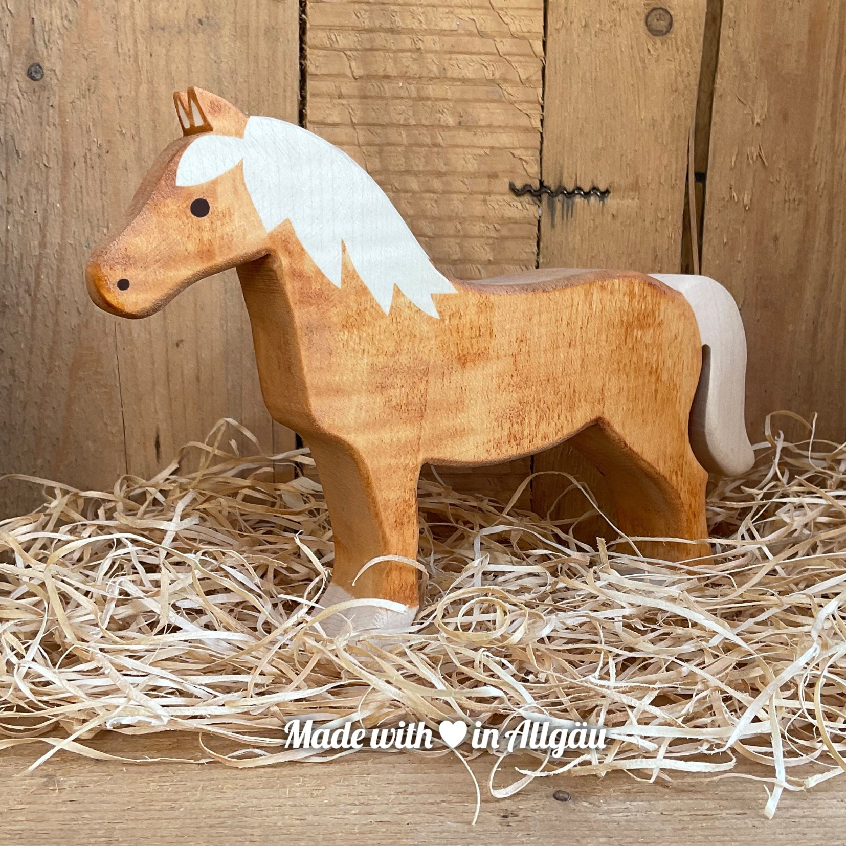 Handgefertigtes Holzspielzeug Pferd Haflinger Stute von Allgäuer Holztiere, stehend auf Holzspänen im Hintergrund raues Holz, aus bayerischem Ahornholz gefertigt, mit pflanzlichen Farben rot-braun bemalt, nachhaltig im Allgäu produziert und für Kinder ab 3 Jahren geeignet.