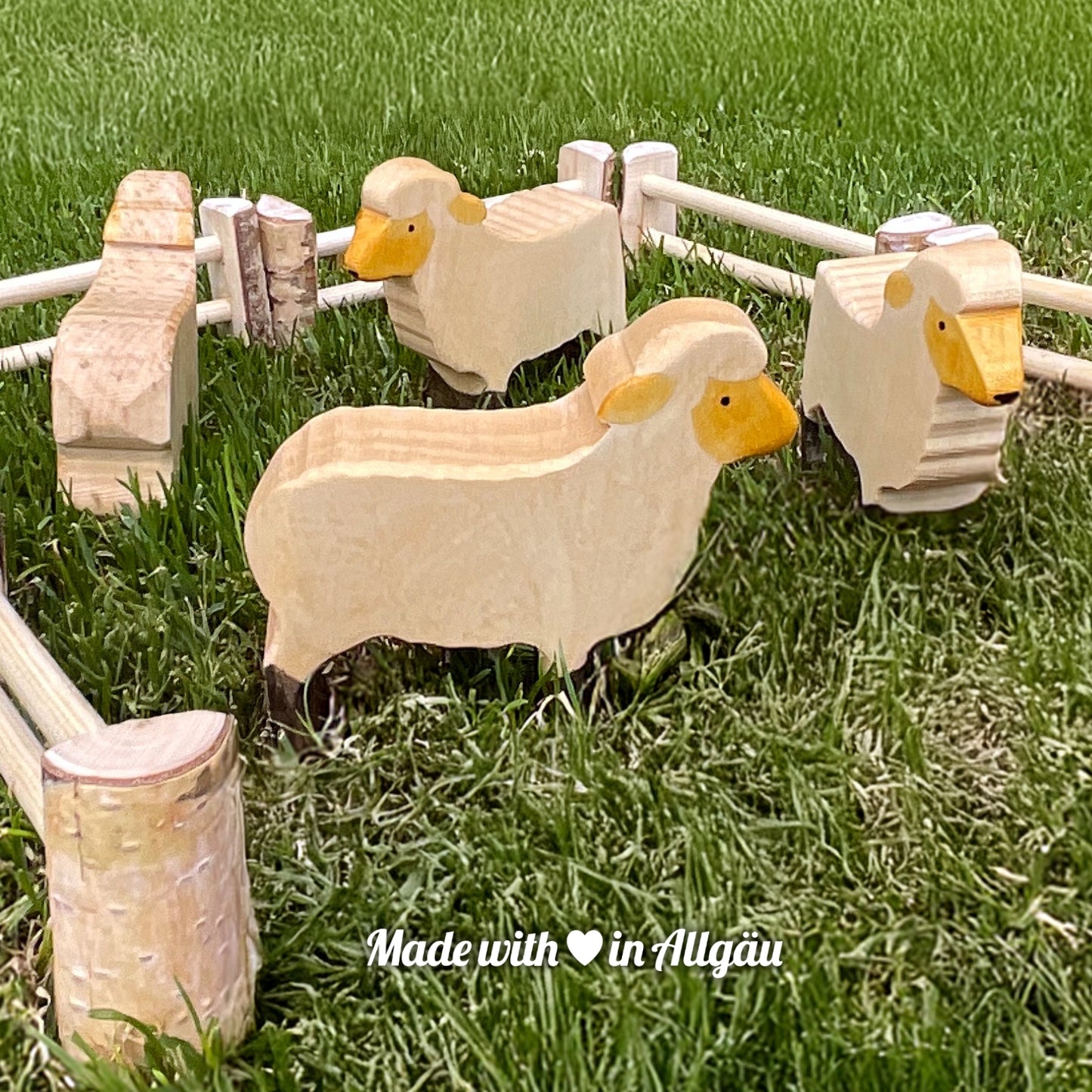 Handgefertigtes Holzspielzeug Schaf Aue weiß von Allgäuer Holztiere, orange und schwarz bemalt mit pflanzlichen Farben, stehend auf Weide in natürlicher Umgebung, aus bayerischem Ahornholz gefertigt, nachhaltig produziert im Allgäu und für Kinder ab 3 Jahren geeignet.