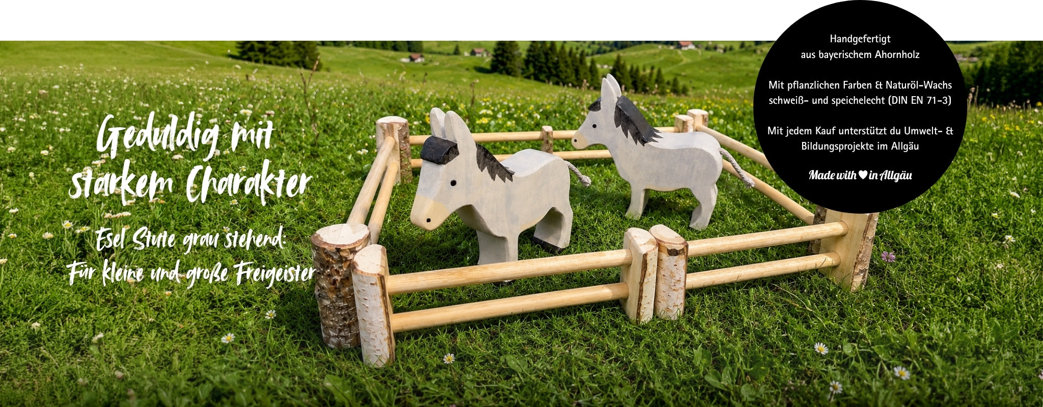 Jetzt entdecken: handgefertigtes Holzspielzeug Esel Stute grau stehend von Allgäuer Holztiere. Zwei graue Esel aus bayerischem Ahornholz stehen auf einer grünen Allgäuer Bergwiese in einem Holzzaun. Mit pflanzlichen Farben bemalt, mit Naturöl-Wachs geschützt, produziert im Allgäu, Made with Love in Allgäu.